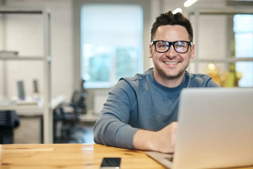 man in long sleeve shirt smiling with glasses looking at you